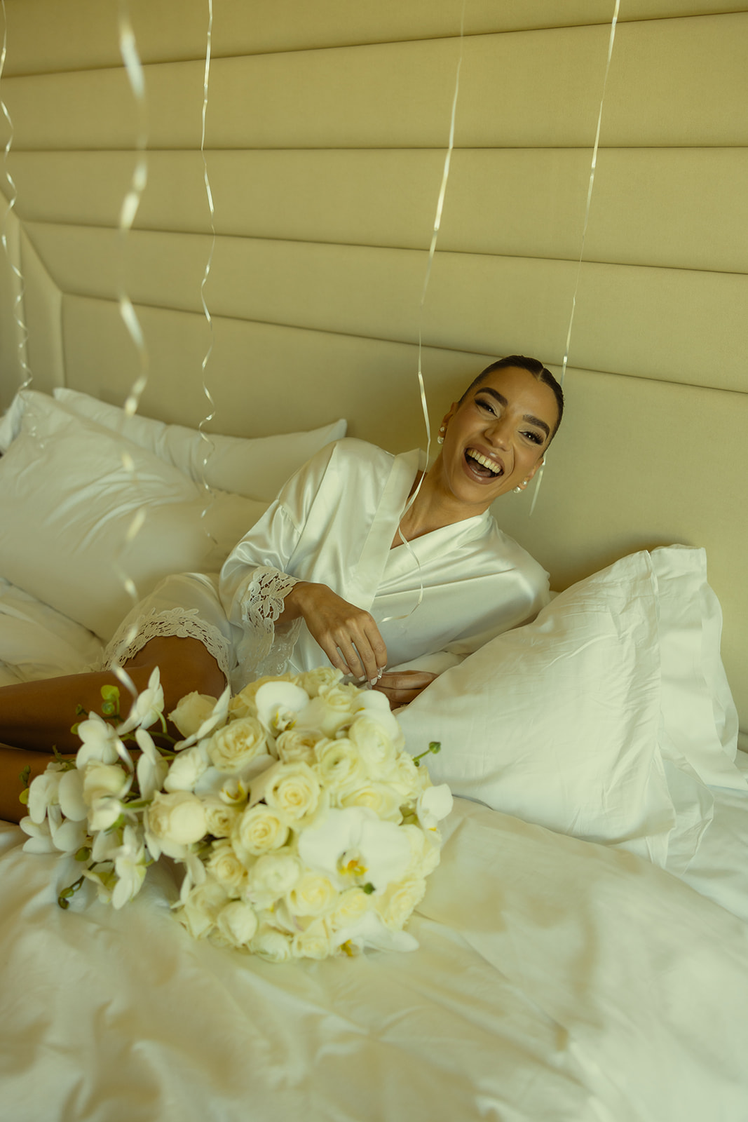 Bride Candid Laughing Portraits in Bride Robe Getting Ready Portraits with her White Roses and White Orchid Wedding Bouquet at JW Miami Turnberry Resort & Spa in Aventura, Florida