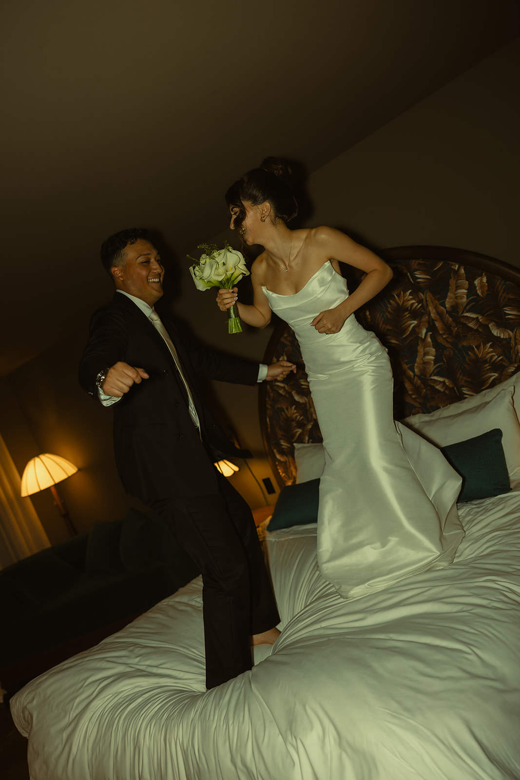 Funky Fun Groom and Bride Jumping in Bed Room Portraits Timeless Wedding in Mayfair Hotel & Garden