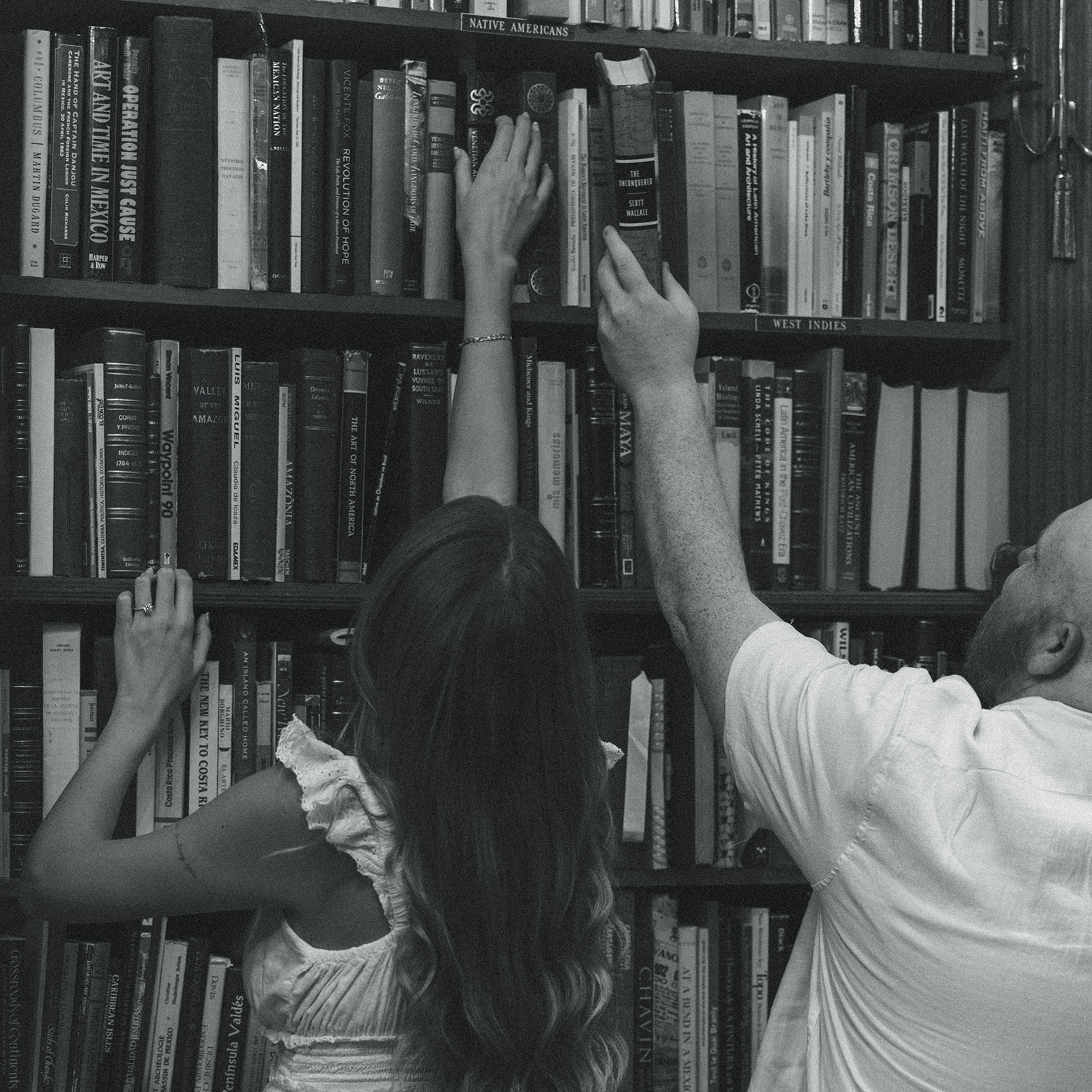 Black and White Historic Bookstore Movie Still Engagement Session Miami Florida Engagement Session Couple Reaching for Books