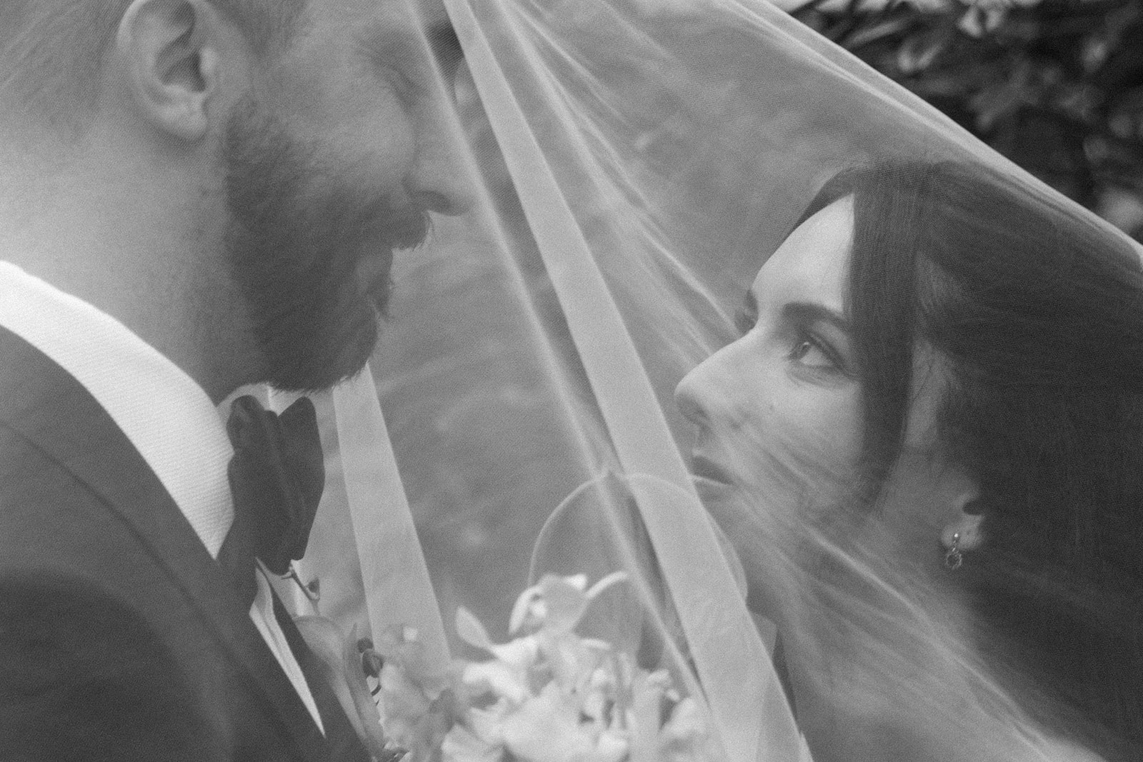A close-up, black and white editorial wedding photograph from a luxurious New York City wedding day, showing a bride and groom looking into each other's eyes, softly framed underneath the bride's sheer tulle veil.
