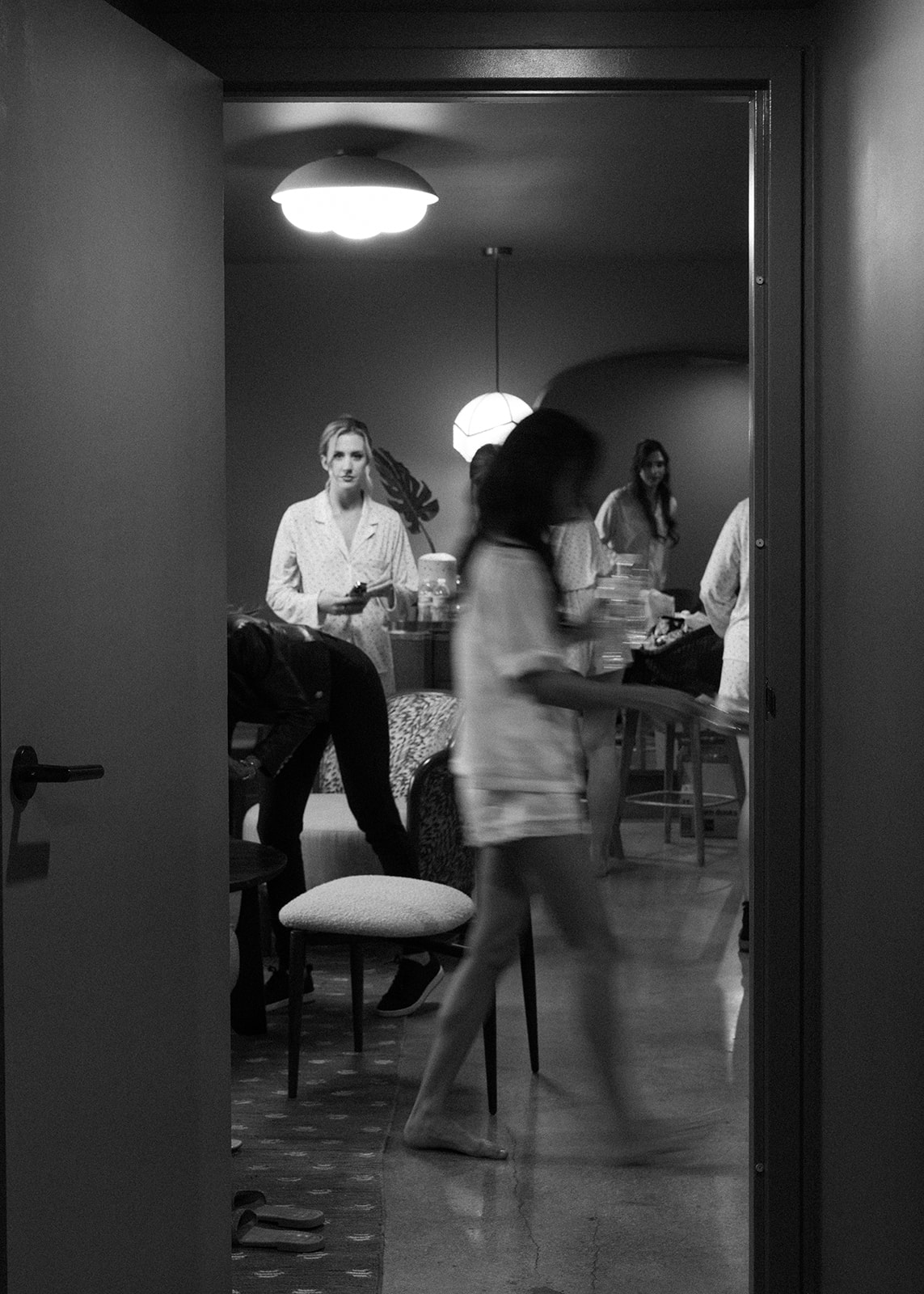 A black and white behind-the-scenes moment from a luxurious New York City wedding day, showing the bridal party preparing inside a softly lit hotel room with candid movement and editorial style composition.