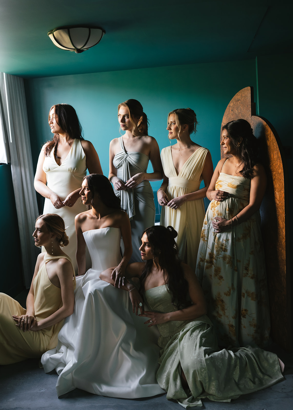 A styled bridal party portrait from a luxurious New York City wedding day, featuring bridesmaids in elegant gowns gathered together in soft natural light beside a window.